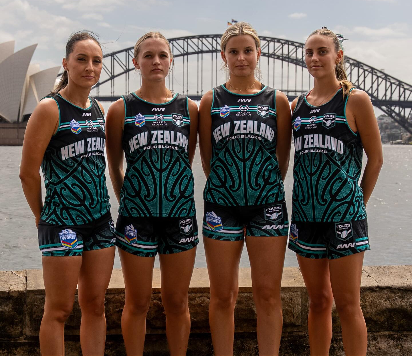 Four women in New Zealand sports uniforms standing in front of the Sydney Opera House and Sydney Harbour Bridge.